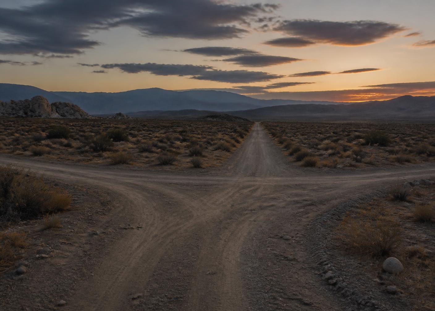 Dirt road crossing empty California desert acreage at dusk